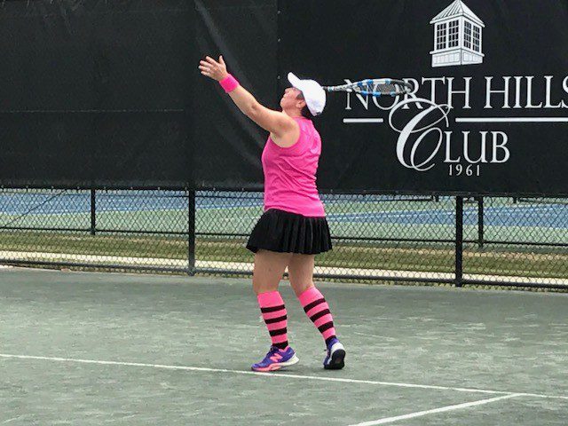 A woman in pink shirt and black skirt playing tennis.